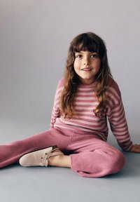 Pull en maille rayé rose et pantalon tapered assorti. Tissu doux et texturé. Chaussures beiges à enfiler avec une bride décorative et un détail de bouton.
