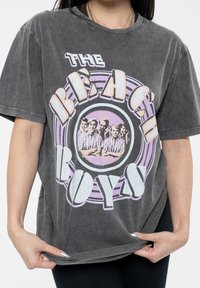 Grey oversized t-shirt with a faded graphic print reading "THE BEACH BOYS," featuring circular accents and a group photo in the center.