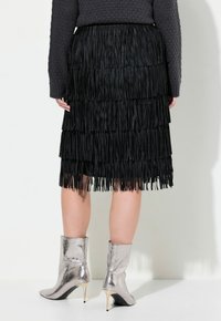 Jupe frangée noire avec plusieurs couches et une finition texturée, associée à des bottines argentées métalliques à bout pointu et talon aiguille.