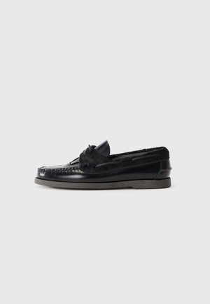 Mocasines de cuero negro con un acabado suave, cordones decorativos y un borde de piel texturizada a lo largo del cuello. Presenta una suela plana de goma.