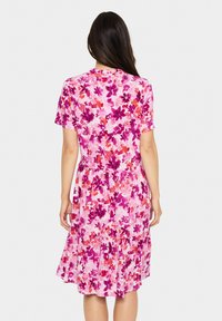 Rochie cu imprimeu floral, cu mâneci scurte, guler rotund și fustă evazată. Predominant roz, cu accente de mov și portocaliu.