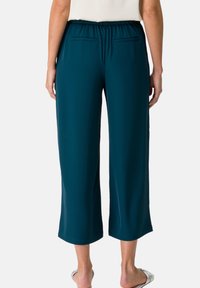 Teal cropped pants with an elastic waistband and two back pockets, featuring a smooth texture and wide legs that end above the ankle.