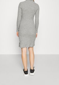 Abito grigio a coste con maniche lunghe e colletto alto, dotato di spacchi laterali e una silhouette aderente, abbinato a sneaker nere.