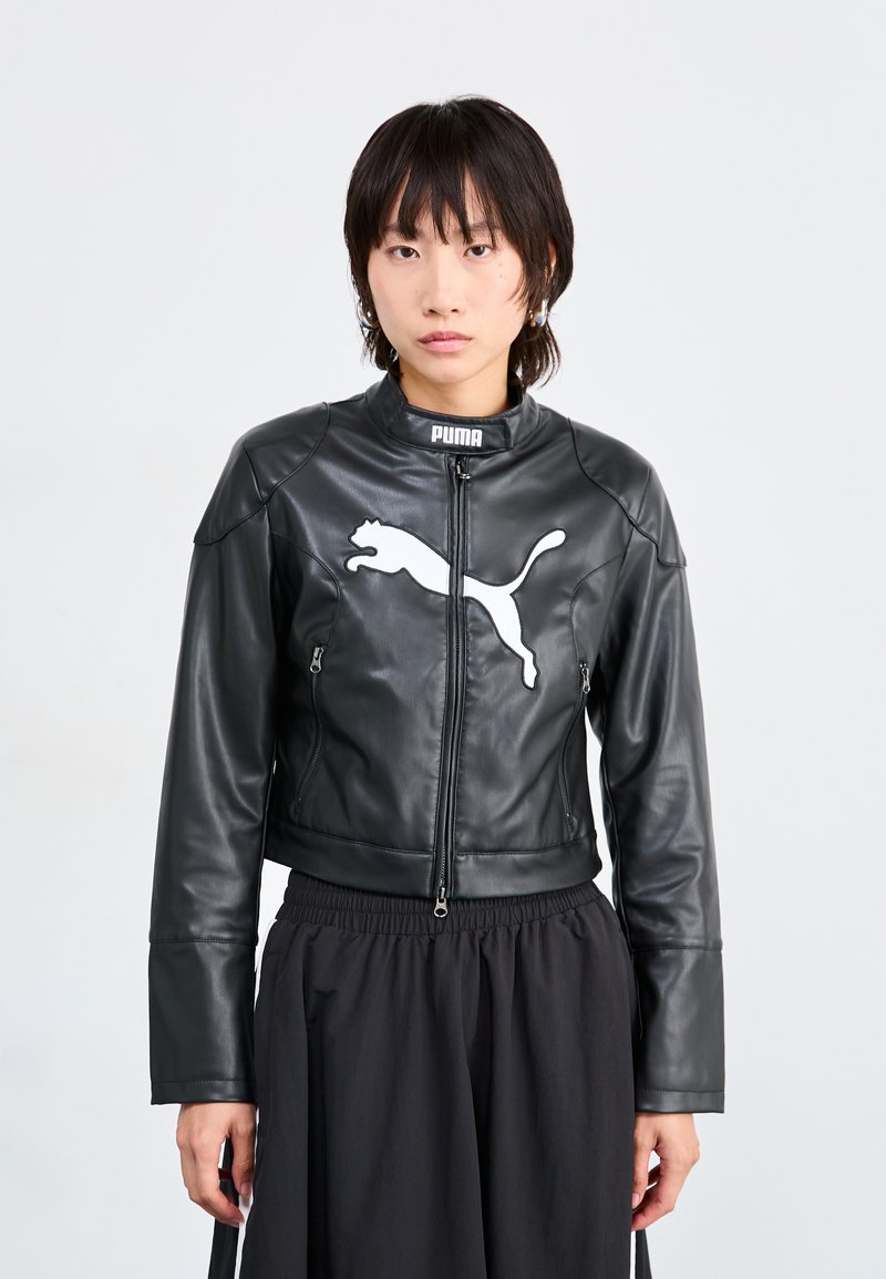 Veste en cuir noir, raccourcie, avec col montant, présentant un grand logo Puma blanc sur la poitrine et deux poches zippées à l'avant.