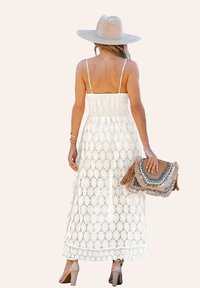 Weißes Maxikleid aus Spitze mit verstellbaren Trägern, strukturiertem Oberteil, geometrischen Mustern und einer fransigen Handtasche. Kombiniert mit einem Hut mit breiter Krempe.