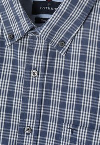 Knoopshirt in marineblauw met een wit ruitpatroon, voorzien van een kraag, knopen en een geborduurd logo op de zak.