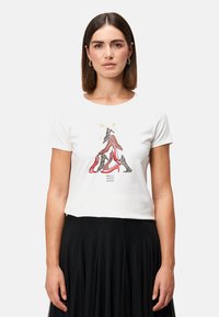 T-shirt blanc à manches courtes avec un graphique de talons hauts rouges et imprimé léopard, accompagné de texte en dessous, associé à une jupe noire.