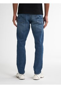 Jeans de mezclilla azul con corte recto, que cuentan con dos bolsillos traseros y una textura desgastada. Combinados con zapatillas blancas.