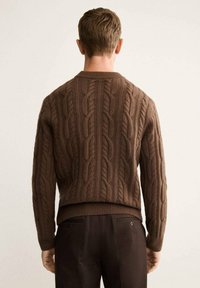 Maglione marrone a maglia cable con scollo rotondo e orlo a coste, caratterizzato da motivi testurizzati. Il maglione è corto e aderente in vita.