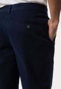 Pantaloni in cotone blu navy con una texture liscia, dotati di una tasca posteriore chiusa da un bottone e un design a vestibilità rilassata.