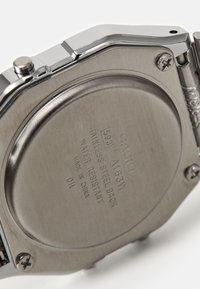 Fond de montre en acier inoxydable, en forme octogonale, gravé des détails de marque et de modèle. Résistant à l'eau avec un système de fermeture par vis. Surface texturée.