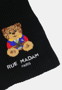 Il tessuto nero a coste presenta un orsetto ricamato vestito con un abito blu e rosso, con "RUE MADAM PARIS" ricamato in bianco sottostante.