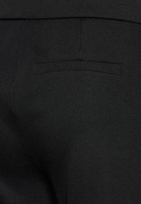 Svarta byxor med en strukturerad tyg, slät midjeband och en bakficka med en smal horisontell öppning.