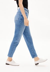 Vaqueros de mezclilla azul claro con corte slim, cinturilla de altura media y dobladillo a la altura del tobillo, combinados con zapatos blancos de cordones.