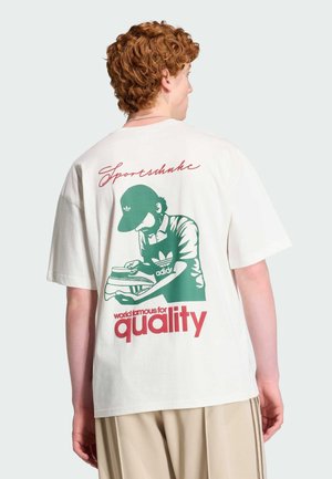 Jeune personne aux cheveux roux bouclés portant un t-shirt blanc avec un graphisme vert représentant une personne cirant une chaussure et un texte rouge "Sportschuhe" et "quality."