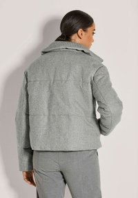 Grijze, gestructureerde jas met een hoge kraag en verlaagde schouders. Kenmerkt zich door een boxy snit en zichtbare naden op de rug.