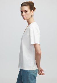 T-shirt bianco a maniche corte con scollo a V, realizzato in cotone, con una vestibilità comoda e un design minimale, abbinato a jeans in denim blu chiaro.
