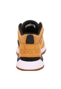 Dzeltena sporta apava ar melniem akcentiem; teksturēts augšdaļa, stingrs papēža balsts un balta zolīte. "Timberland" iespiests uz papēža.