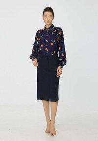 Blouse à motifs floraux en marine avec des fleurs colorées, associée à une jupe crayon noire. Comporte un col, un devant boutonné et des manches bouffantes.