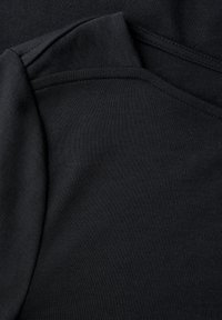 Nahaufnahme von übereinanderliegenden schwarzen Baumwollstoffen mit sichtbaren Nähten und feiner Strickstruktur.