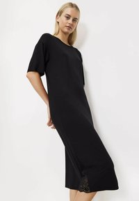 Czarna sukienka o luźnym kroju, z krótkimi rękawami i długości sięgającej kolan. Charakteryzuje się koronkowym wykończeniem wzdłuż bocznego szwu dla dodatkowego akcentu.