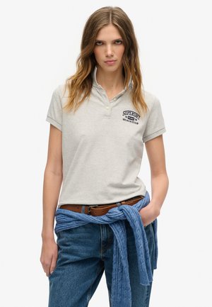 Grå polo T-shirt med krave og broderet "SUPERDRY BEACH CLUB" logo, parret med blå jeans og en blå striktrøje knyttet om taljen.