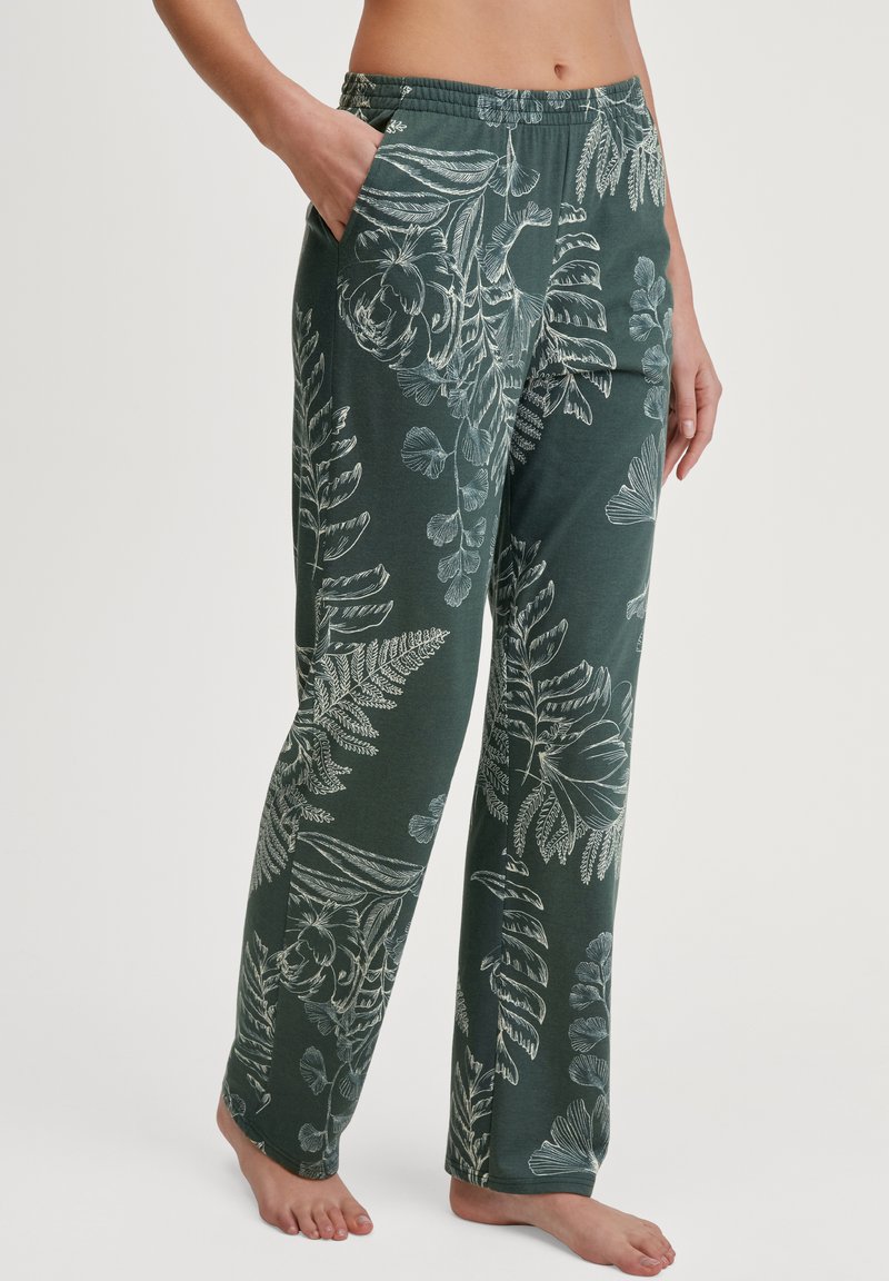 Grüne Hose mit elastischem Bund, die ein weißes botanisches Muster mit Blättern und Blumen aufweist. Hergestellt aus weicher Materialqualität und ausgestattet mit seitlichen Taschen.