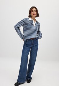 Polo a maniche lunghe a righe blu navy e bianche con colletto bianco, abbinato a jeans in denim blu a gamba larga e scarpe nere.