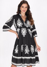 Rochie neagră cu modele abstracte albe, decolteu �în V, mâneci trei sferturi și tiv cu volane în straturi. Textură de țesătură netedă.
