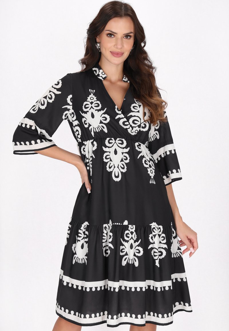 Rochie neagră cu modele abstracte albe, decolteu în V, mâneci trei sferturi și tiv cu volane în straturi. Textură de țesătură netedă.