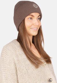Braune, gestrickte Mütze mit einer gerippten Struktur und einer kleinen, aufgestickten Smiley-Gesichtsverzierung auf der Vorderseite. Das Design ist eng anliegend und lässig.