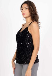 Débardeur en sequins noirs avec un décolleté en V, des fines bretelles et une coupe ample. La texture est brillante, avec une surface lisse et des détails scintillants.