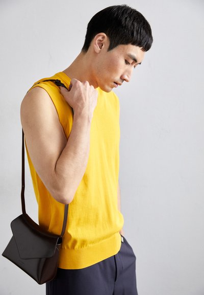 Yellow sleeveless sweater with ribbed hem, paired with a dark brown leather crossbody bag featuring an angular flap design.