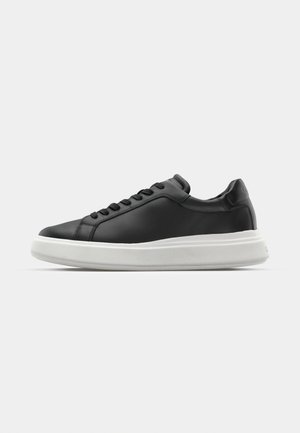 Black leather sneaker with a smooth finish, white rubber sole, rounded shape, six eyelets for laces, and subtle branding on the heel.