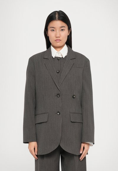 Blazer gris a rayas con un corte entallado, diseño de doble botonadura, botones negros y solapas con muescas. Combinado con una camisa blanca de cuello.