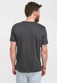 Camiseta gris oscuro, de manga corta, cuello redondo. Textura de tela suave, con costuras visibles y dobladillo recto. Vista trasera.