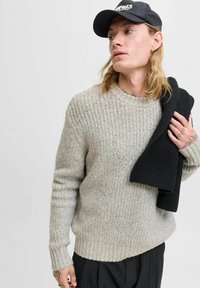 Suéter gris de punto con un patrón texturizado, cuello redondo y puños de canalé, combinado con una bufanda negra sólida. Diseño unisex, tejido suave.