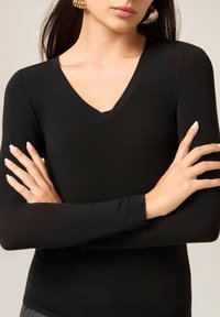 Czarna, dopasowana bluzka z długim rękawem i dekoltem w serek, o gładkiej fakturze. Akcesoria to duże kolczyki-koła.