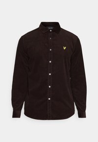 Camisa de pana marrón con cuello puntiagudo, botones frontales y un pequeño logo amarillo en el pecho. Mangas largas con puños abotonados.