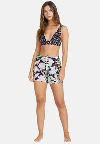 Svart blomsterbikini topp med dyp V-hals og brede stropper, kombinert med høyt liv shorts med et dristig rosa og grønt blomsterdesign.