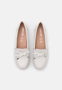 Zapatos de barco de cuero blanco con punta redonda, cordones laterales y un lazo decorativo. Presentan una superficie suave y detalles de costura sutiles.