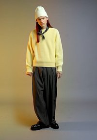 Valkoinen ribattu neule, löysät harmaat raitahousut, mustat platform-kengät ja valkoinen pipo, musta huivi solmittuna kaulan ympärille.