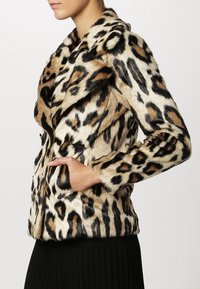Lepelprint faux fur jas met een notch-kraag, twee voorkruiszakken en een aansluitend ontwerp. Kleurenpalet bevat beige, zwart en bruin.