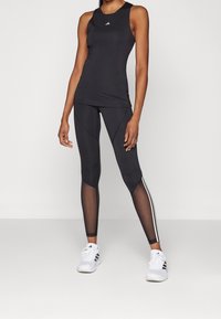 Svart athletisk linne och leggings med en åtsittande design, mesh-detaljer och tre vita ränder längs den yttre benet. Vita sportskor.