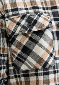 Skjorte i ternet flannel i sort, hvid og beige nuancer med en brystlomme, der har to sorte knapper, og en blød tekstur.
