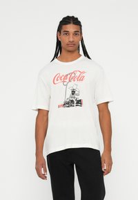 Valge puuvillane T-särk, millel on graafiline kujutis cowboy'st Coca-Cola pudeliga. Lühikesed varrukad, mugav lõige ja ümar kaelus.