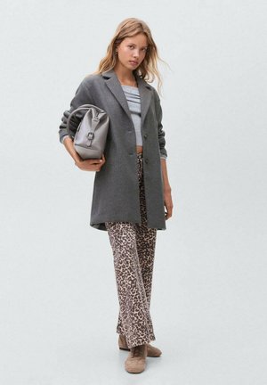Grau übergroßer Blazer, hellgraues Cropped-Top, beige Hose mit Leopardenmuster und beige Schuhe. Graue Umhängetasche in runder Form.