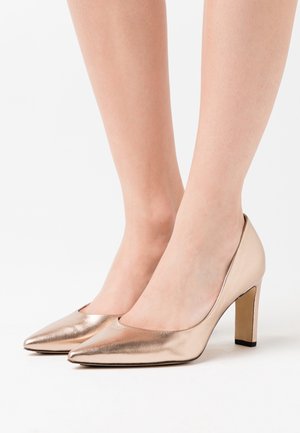 Chaussures à talons hauts en rose gold métallique avec un bout pointu et une texture lisse. Les talons sont cylindriques et mesurent environ 5 cm de hauteur.