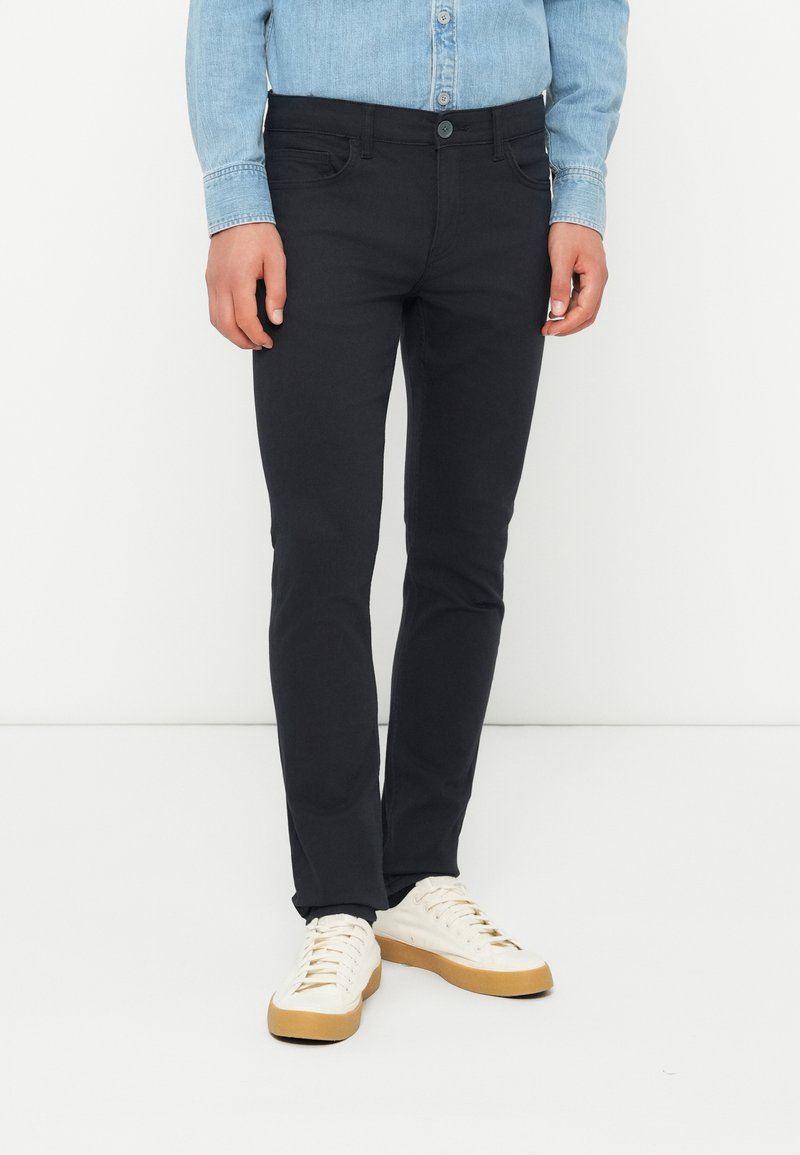 Slim-fit svarte bukser laget av bomullsmiks, med knappeåpning, belteholdere og frontlommer, kombinert med hvite sneakers.