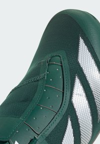 Green athletic shoe featuring a textured upper, streamlined design, synthetic material, and white accents with a mesh pattern.